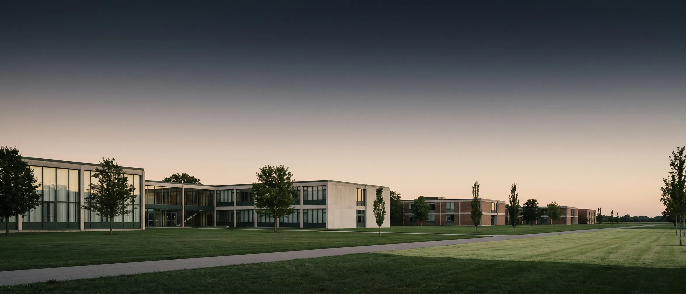 Un campus vacío al atardecer, con un camino cruzando el pasto